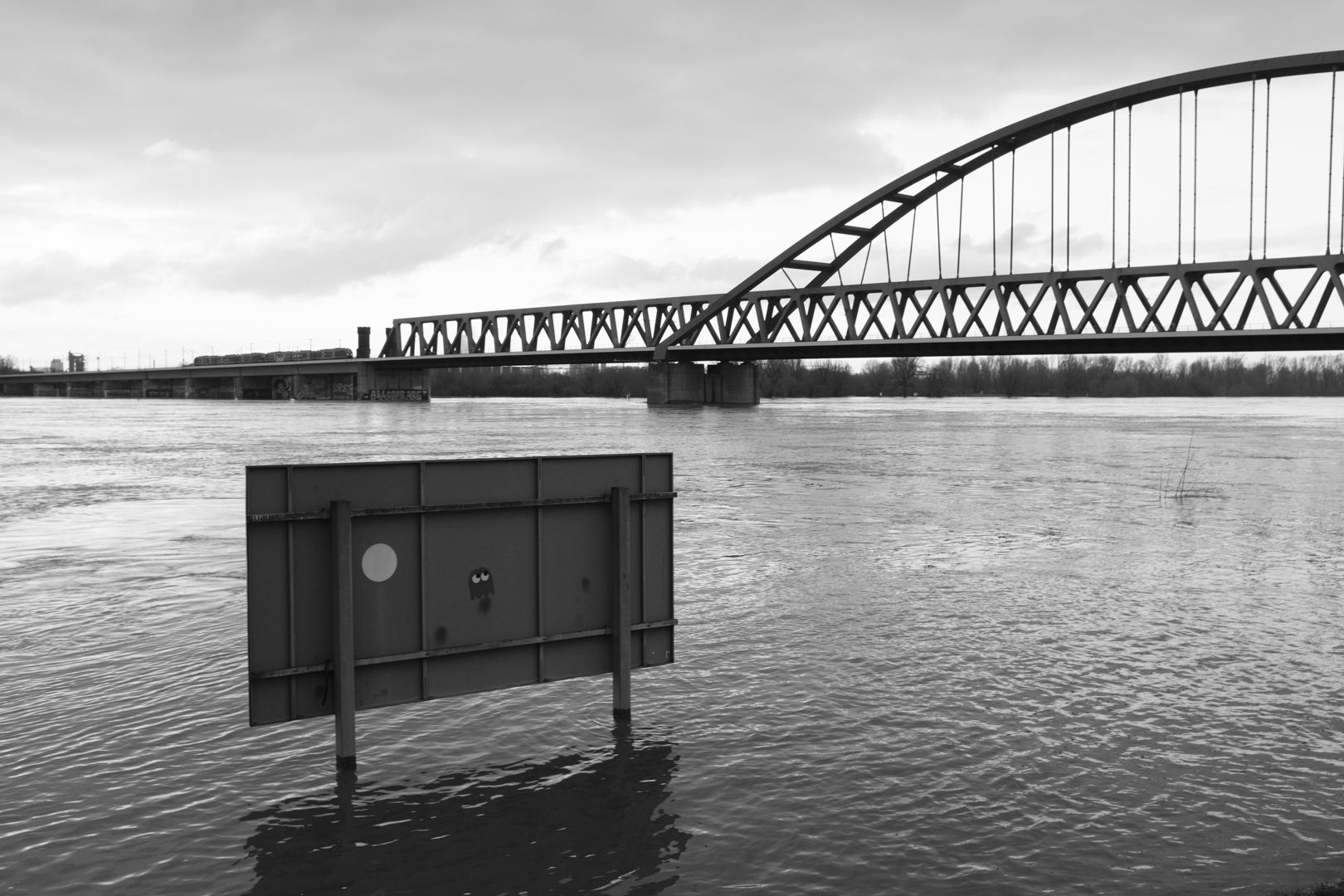 Pac-Man-Aufkleber auf der Rückseite eines großen Schildes im Fluss vor einer Eisenbahnbrücke